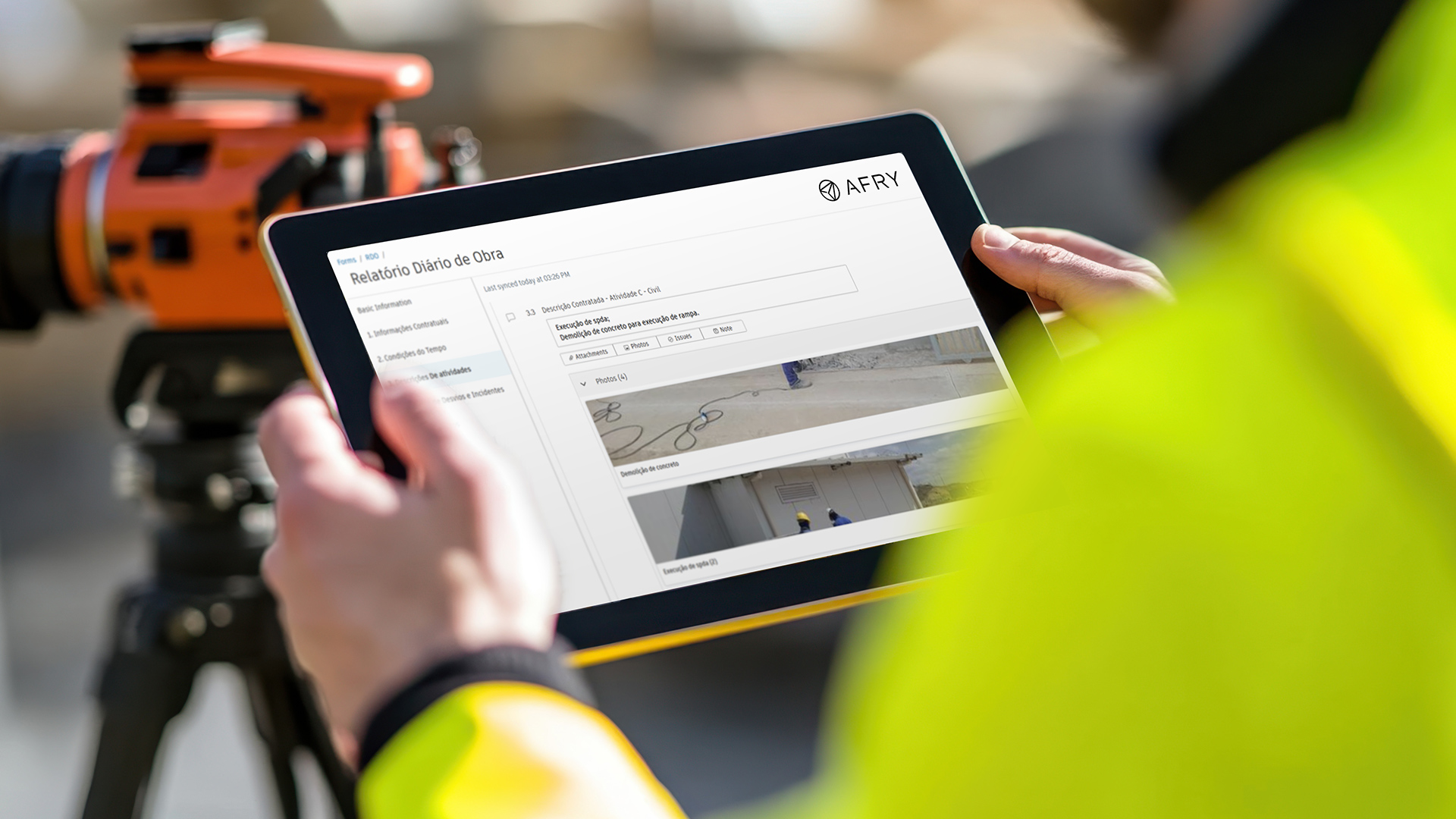 Person in high-visibility jacket holding a tablet showing a form with a photo and text, with an orange surveying instrument in the background