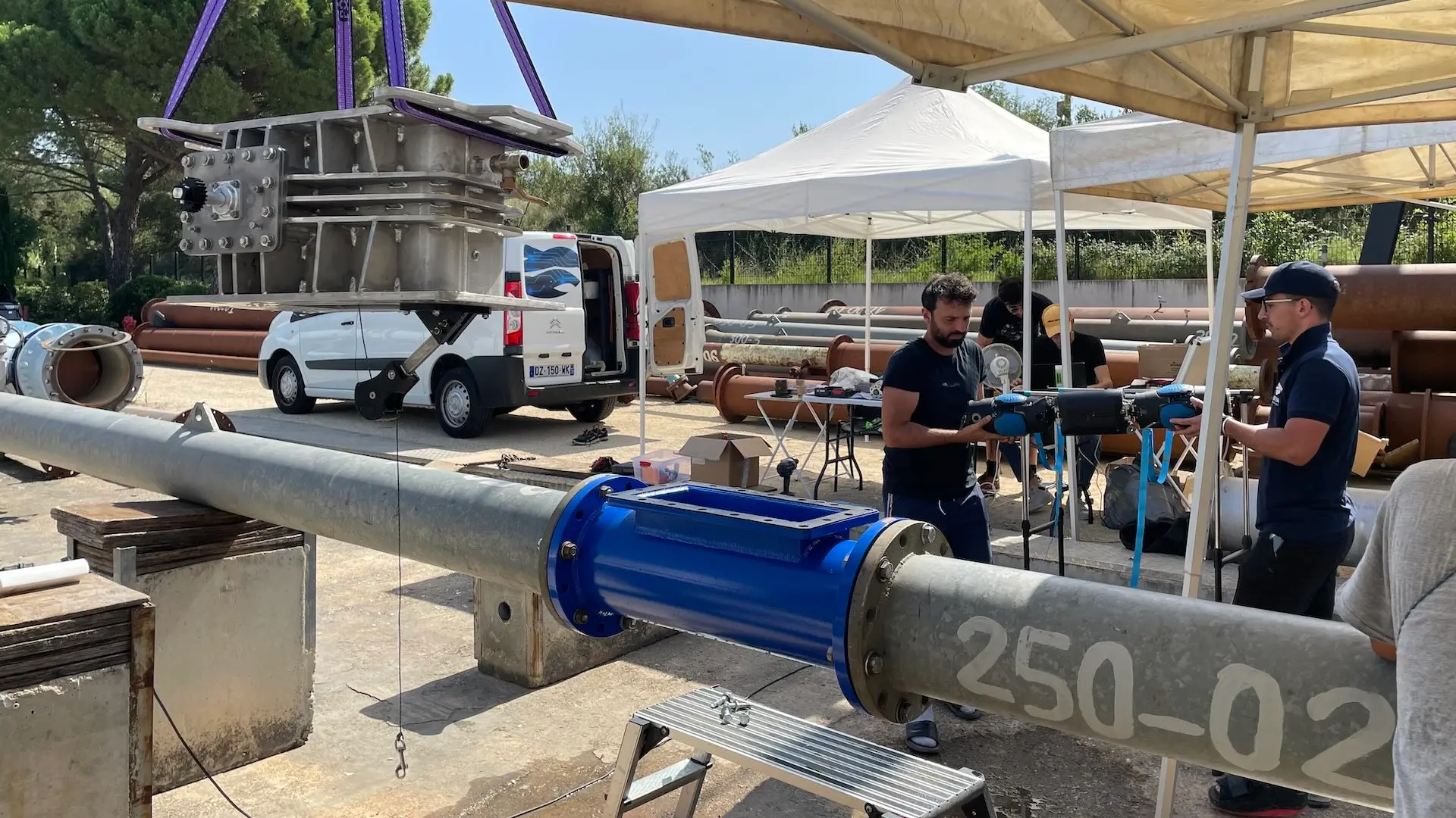 Two engineers carry a preproduction model of ACWA’s autonomous robot to a large pipe set up above ground for testing.