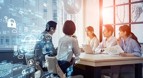 People at work collaborating around a table and a computer with a graphic overlay of data