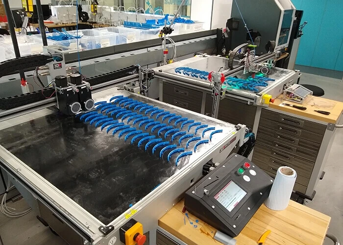 Rows of 3D printed blue face shield holders lined up on a table.