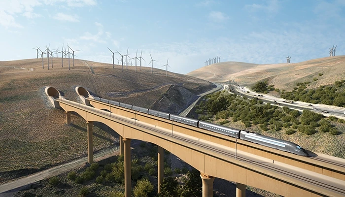 A train goes through a tunnel on a hillside, with wind turbines in the background.