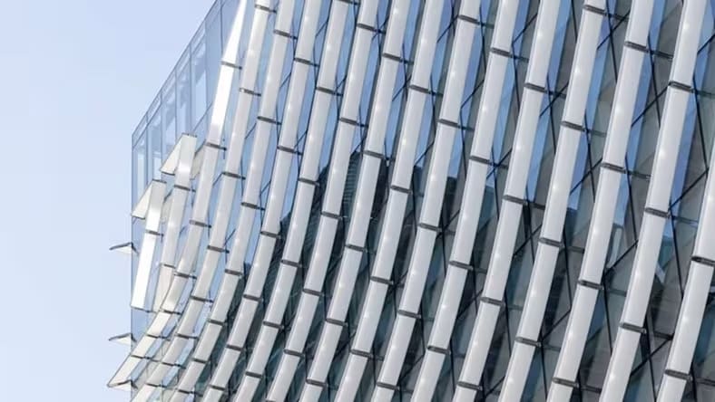 A close-up of a building facade shows undulating waves of aluminum and glass.