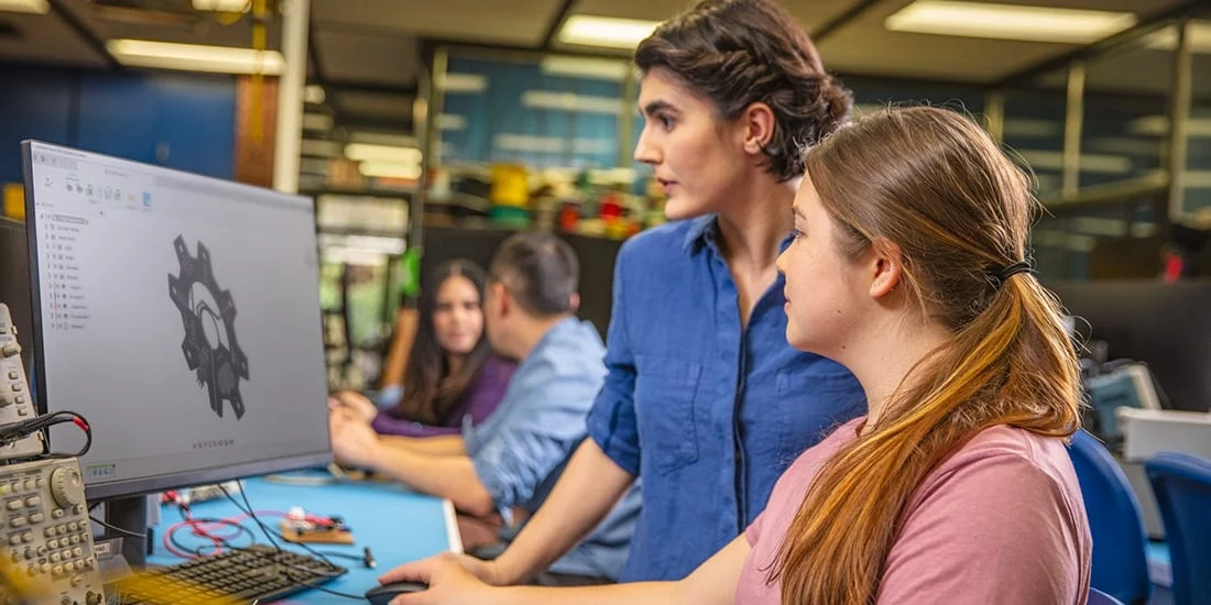 Two women in a workshop look at a computer monitor
