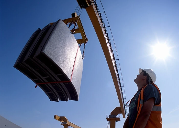 A crane lifts precast panels while a construction worker looks on.