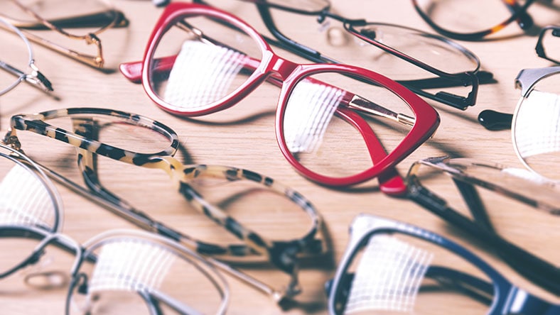 A group of eyeglasses is shown on a wood background.