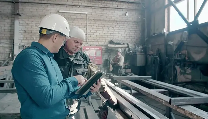 Two men in a construction setting look at a tablet.