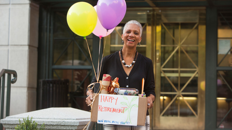 Woman carrying belongings with happy retirement sign and balloons