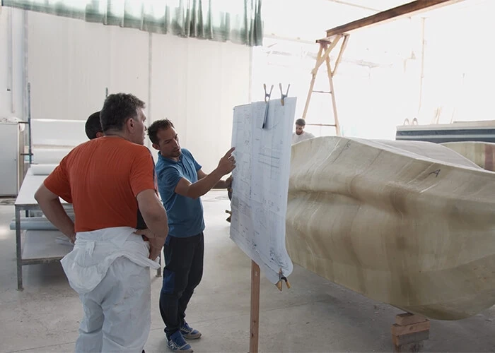 Three men look at 3D-printed boat designs.