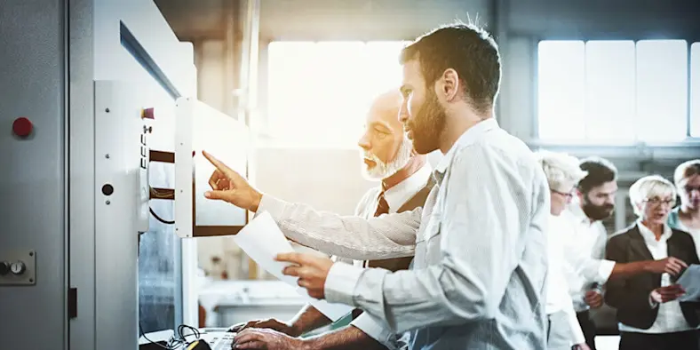 A young worker shows a more seasoned worker some information on a screen.