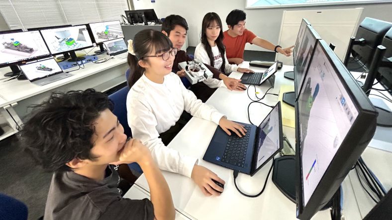 Five students in the smart factory education program at Kogakuin University in Japan sit at computers in a campus classroom, working together on projects.