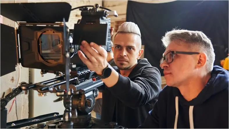 Two men look at the monitor on a professional video camera.