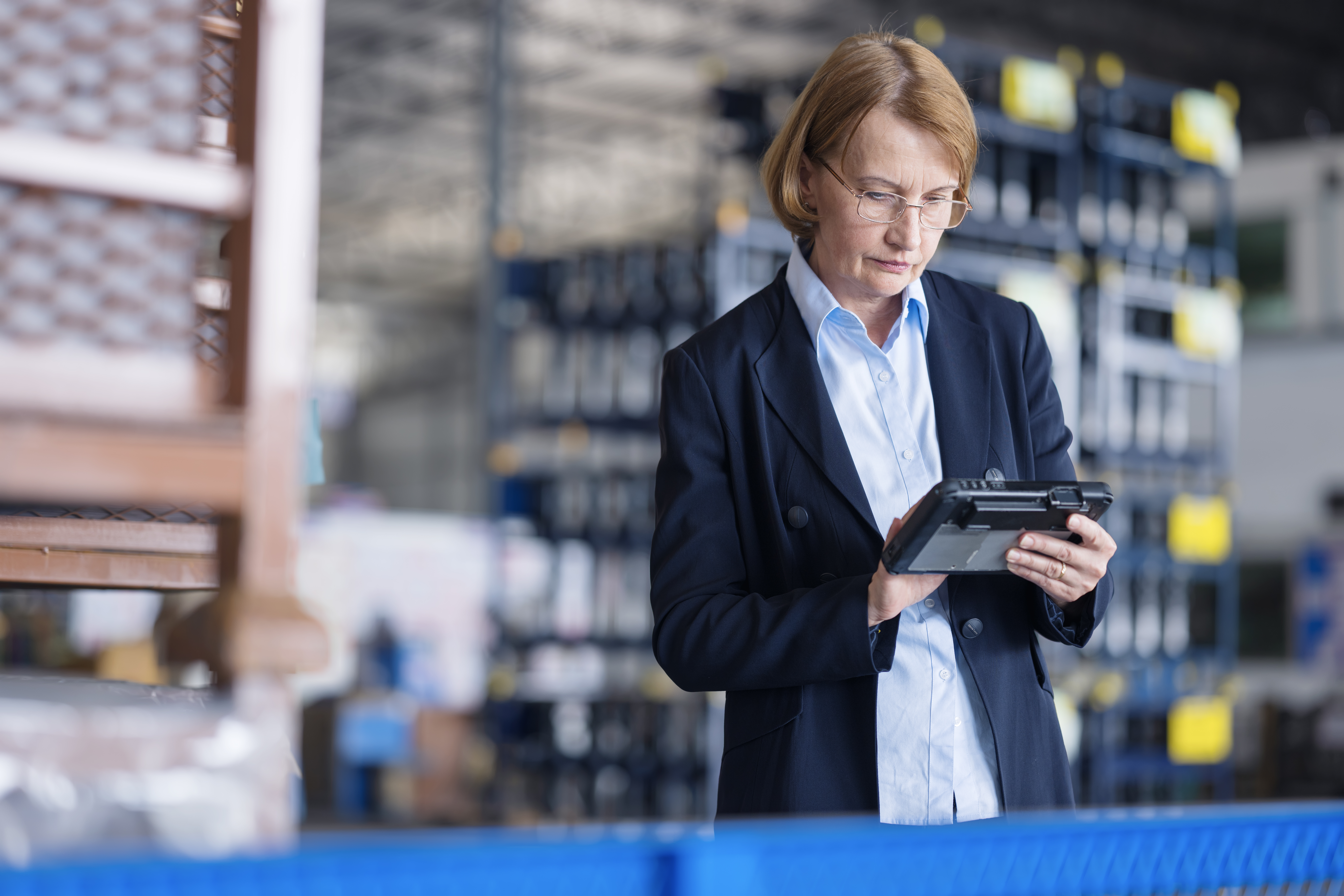 A businesswoman is using a tablet in a warehouse and analyzing inventory data near shelves.
