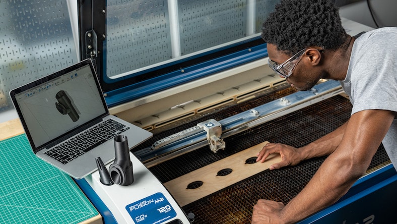 A man examines a design on a laptop while woodworking.