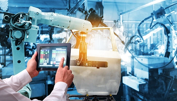 A man holds tablet in front of industrial robots on an assembly line