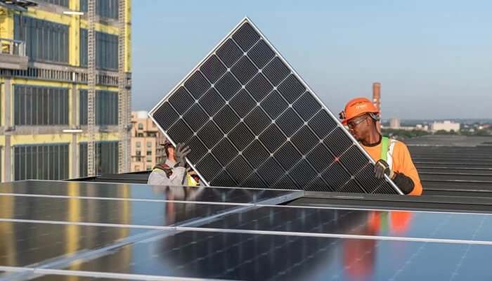 Two men carry a solar panel to a low-carbon development.