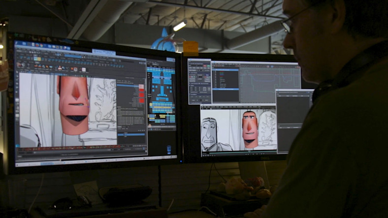 A man sits at a desk in dark profile in front of two computer screens showing animation work