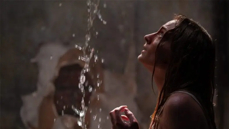 A person standing under a stream of water with a textured wall in the background.