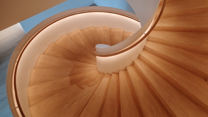 An overhead view of a contemporary spiral staircase shows soft indirect lighting directed on the steps from under the railing.