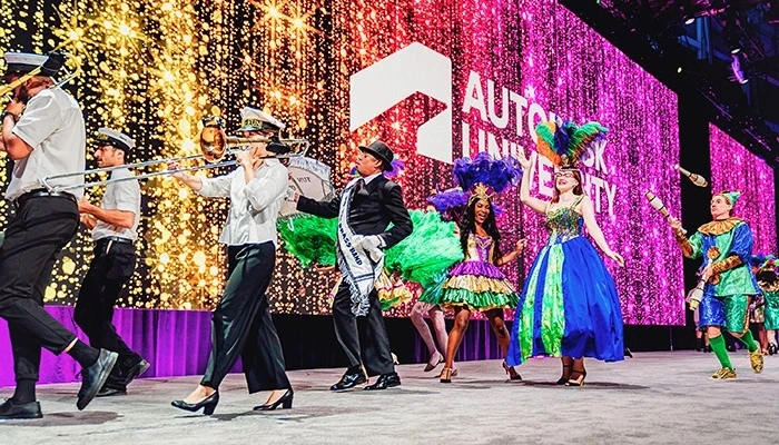 A marching band and dancers in Mardi Gras regalia walk offstage at Autodesk University.