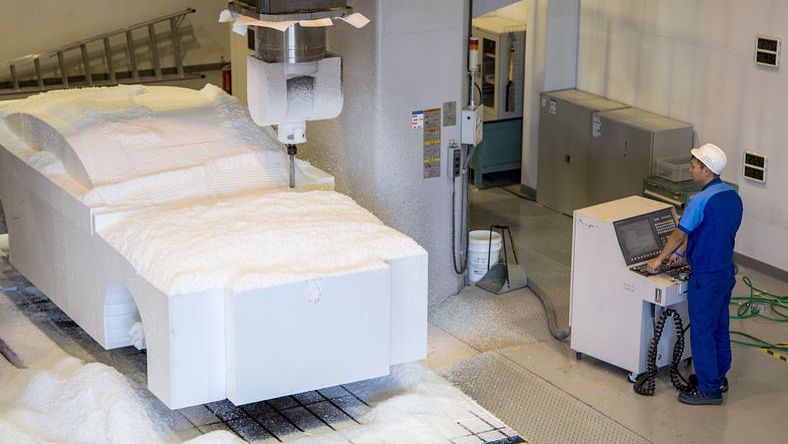 A worker milling a full-sized foam prototype of a car chassis using a CNC machine.