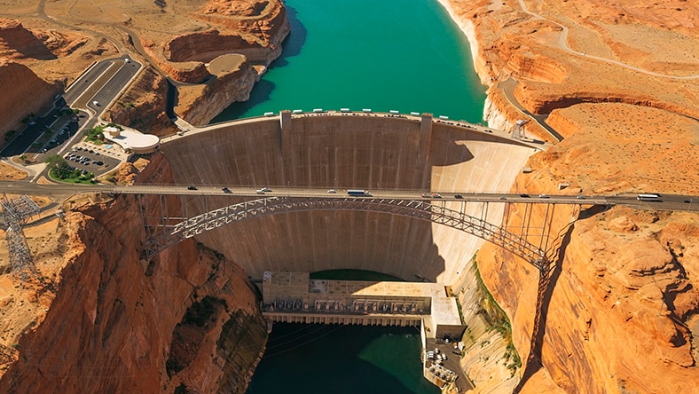 Arial view of a large dam and bridge over a river in an arid landscape.