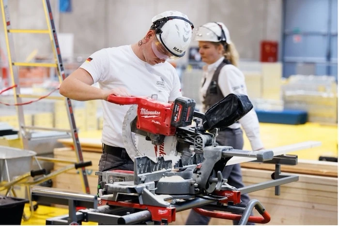 Two people wearing helmets adjust machinery.