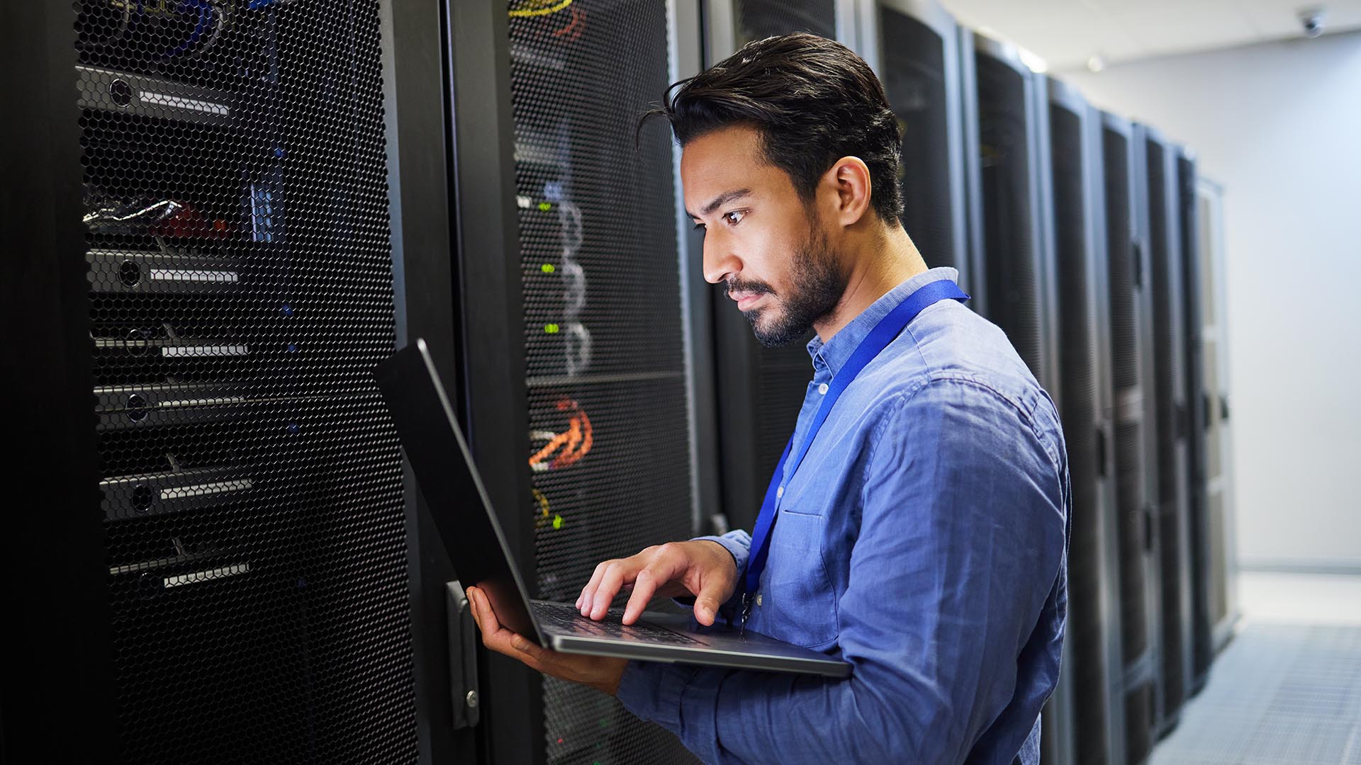 A man in a building’s data center consults his laptop.