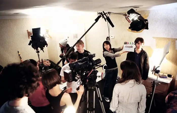A group of people on a movie set with cameras and lights, filming a scene in a room