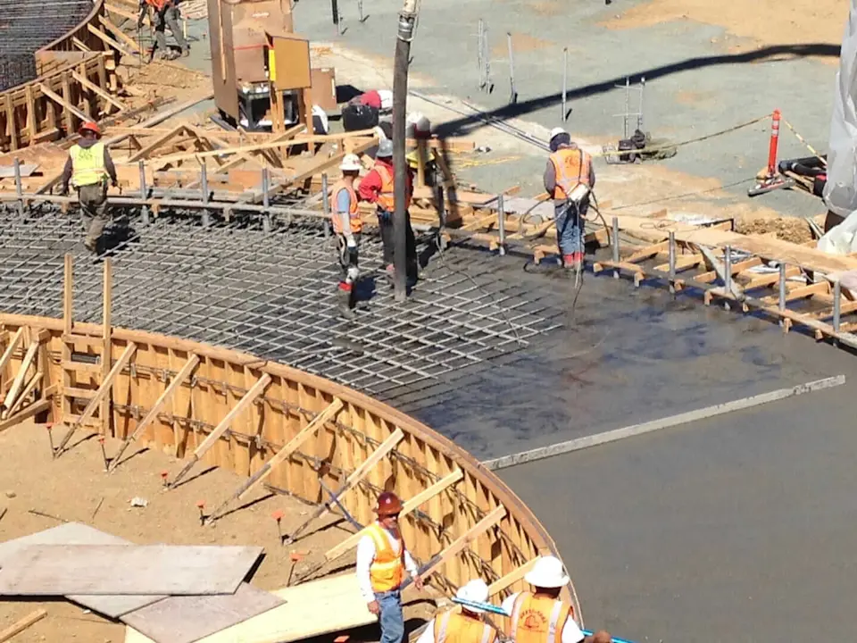 Construction workers pour cement into a form structured with rebar.