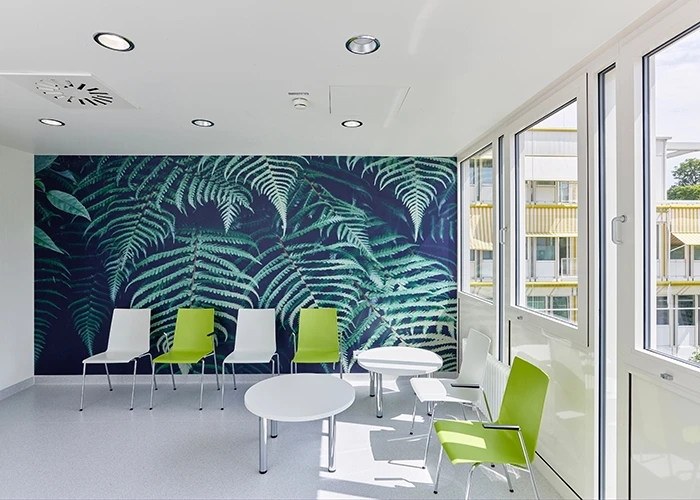 A hospital waiting room with green and white chairs and a leafy accent wall
