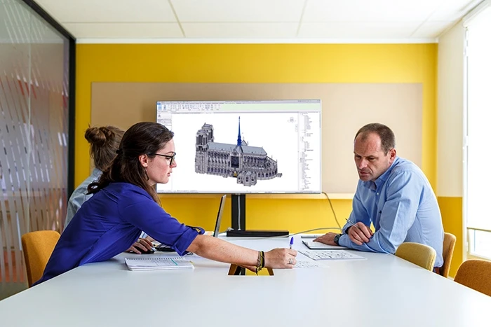 AGP employees around a table discussing the plans for renovation, with a model of Notre-Dame in the background on a computer screen