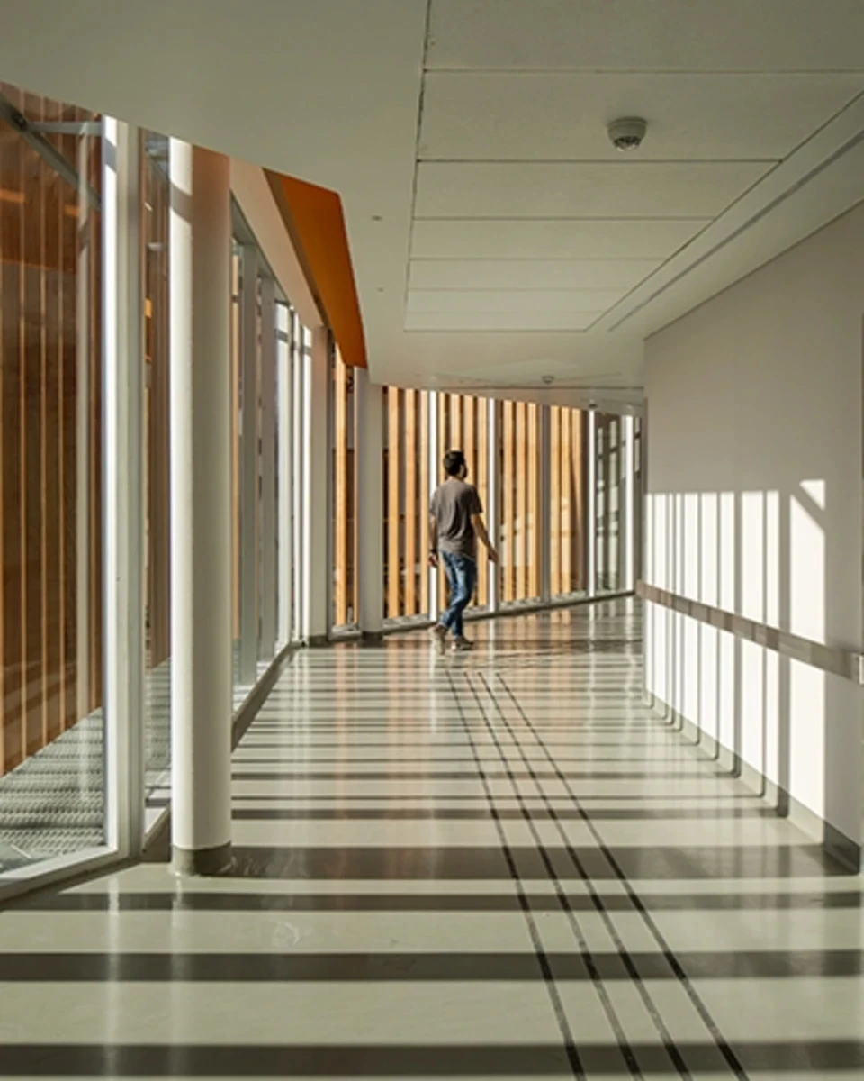 A man walks through a sunlit corridor with striped shadows. 