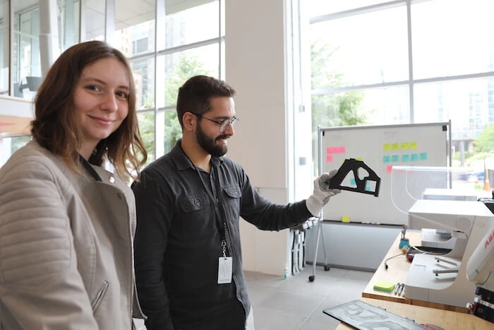 Two people work next to a 3D printer.