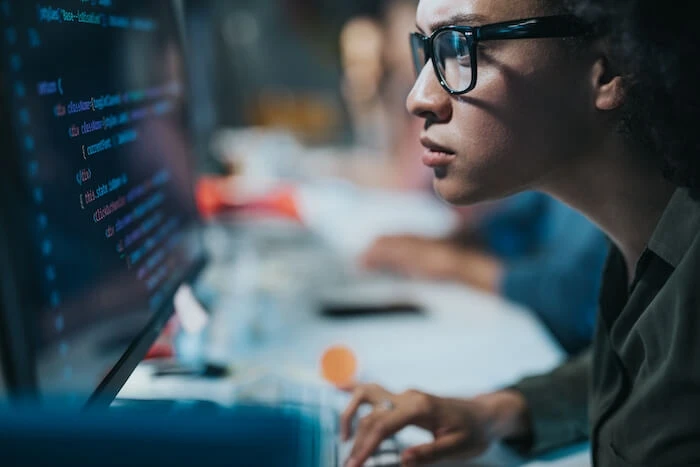 A woman in glasses stares intently at a computer monitor