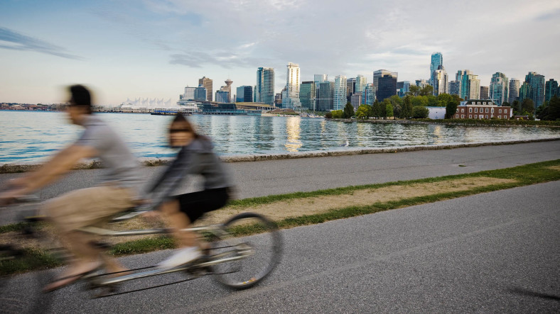 Cyclists on a tandem bike ride along a path with the Vancouver skyline in the background.