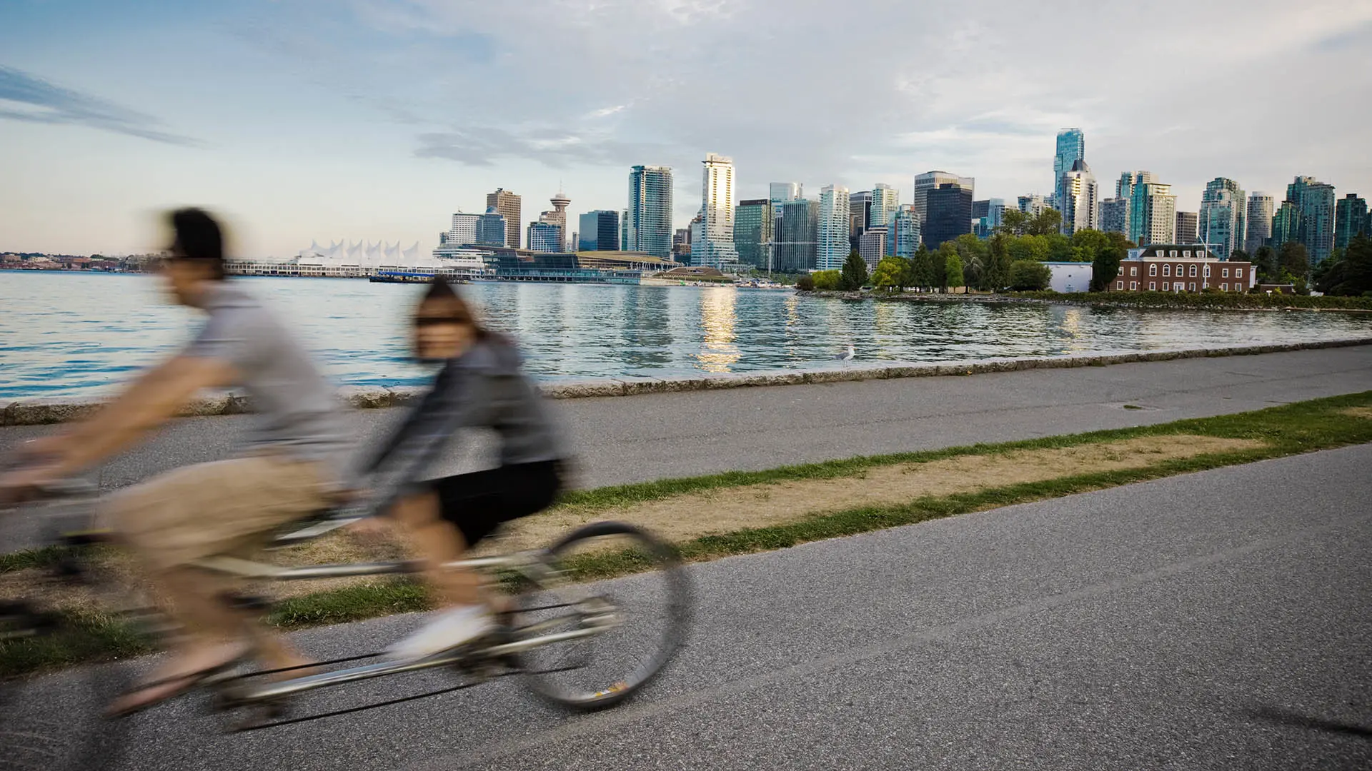 Des cyclistes sur un tandem roulent sur une piste avec l’horizon de Vancouver en fond.