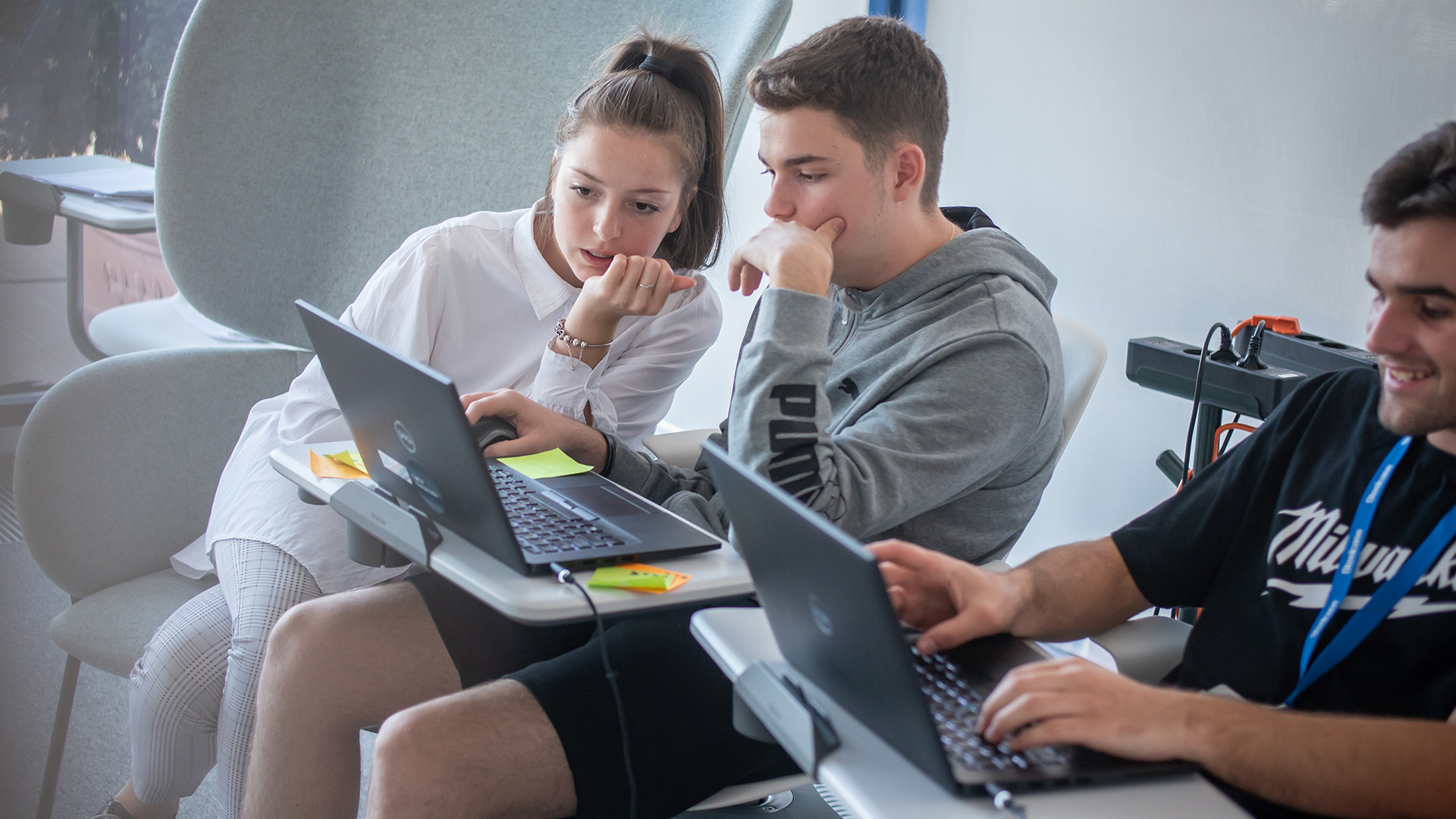 Two teenagers in a classroom look at a laptop together.