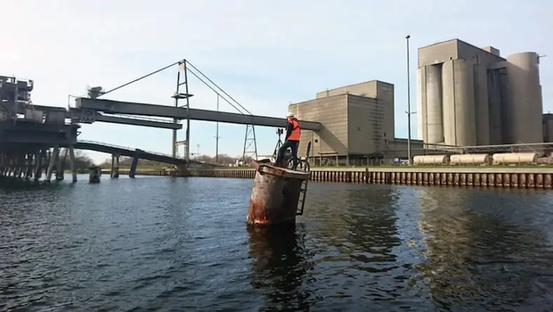 An engineer perched on a pipe-like structure in a river surveys a dangerous industrial site.