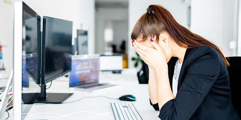 A woman sits at a desk with her head in her hands
