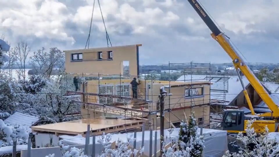 A crane drops in a prefabricated housing component on a snowy day.