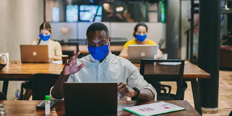 man wearing a mask in front of a laptop during a meeting