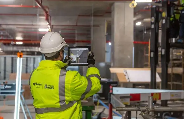 A construction worker checks a building model on a tablet at the jobsite.