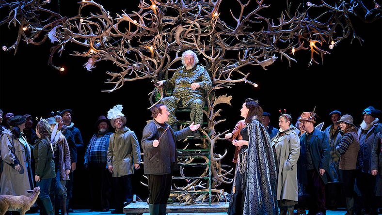 On an opera stage, a man sits on a throne of deer antlers.