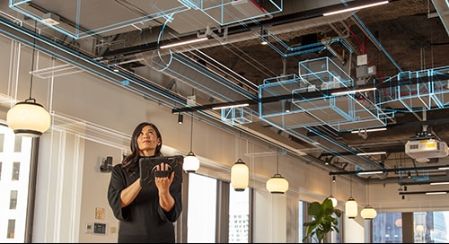 Woman in open cafe space holding tablet and looking at ceiling overlayed with architectural schematics