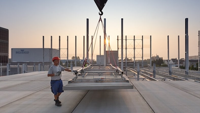 A man in a hard hat places prefabricated building parts at dusk.