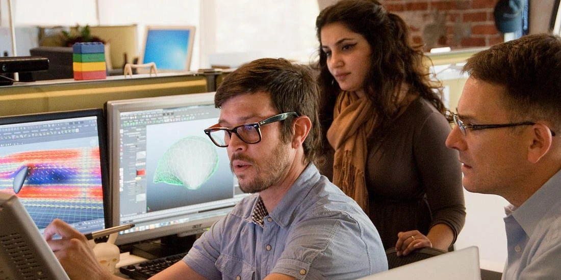 hree people gather around several monitors.