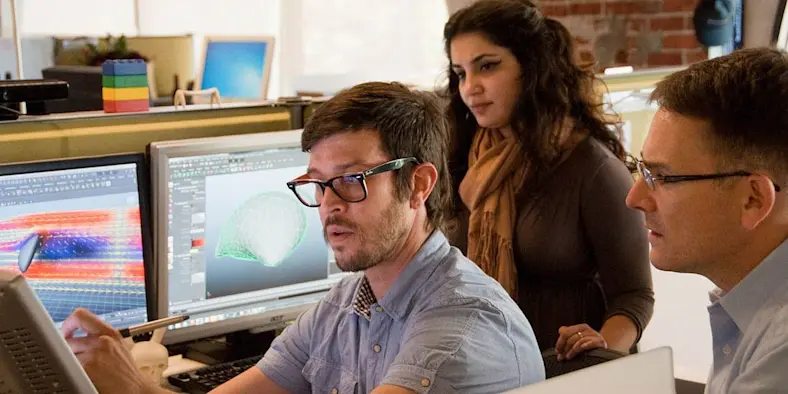 Three people gather around several monitors.