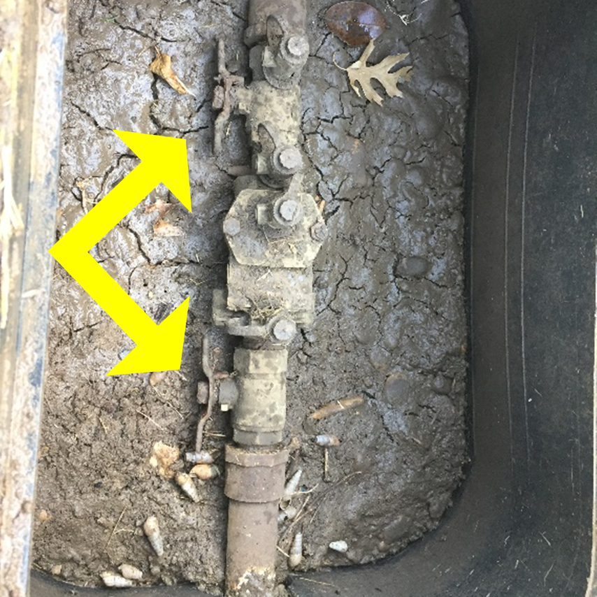 Example of in-ground backflow prevention assembly. One of the two handles, as indicated by yellow arrows, can be turned upright to shut water off to the irrigation system. The backflow assembly and PVC ball valve will typically be located near the water meter in the front yard in a box underground with a green or black lid.  