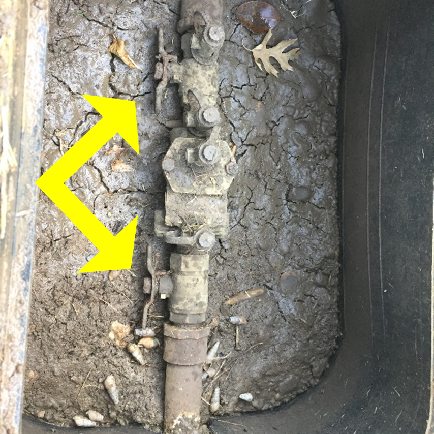 Example of in-ground backflow prevention assembly. One of the two handles, as indicated by yellow arrows, can be turned upright to shut water off to the irrigation system. The backflow assembly and PVC ball valve will typically be located near the water meter in the front yard in a box underground with a green or black lid.