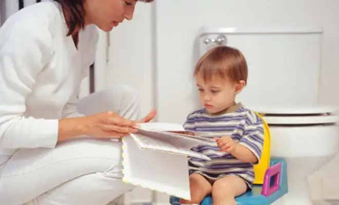 Une maman lit une histoire à son enfant assis sur son pot d'apprentissage de la propreté.